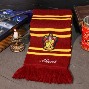 Puede incluir: Bufanda burdeos y dorada con el parche del escudo de Gryffindor y el nombre "Alexis" bordado en blanco. La bufanda tiene rayas doradas y un borde con flecos. Un artículo para fans.