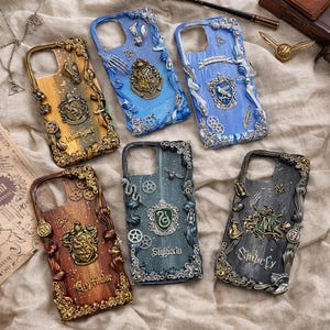 Puede incluir: Seis fundas de teléfono con diseños intrincados. Cada funda presenta una combinación de colores diferente, incluyendo dorado, azul, marrón y gris, con emblemas en relieve y elementos decorativos. Las fundas son probablemente para un modelo de teléfono específico.