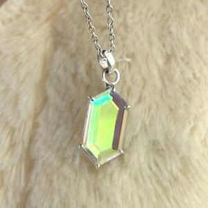 May include: A silver necklace with a pendant featuring a faceted, iridescent gemstone. The pendant has a rectangular shape with multiple facets that reflect green, yellow, and purple hues. The chain is delicate and hangs from the pendant.