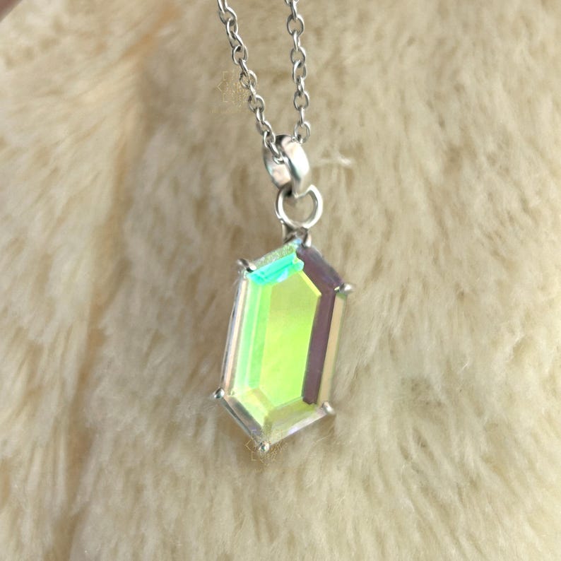 May include: A silver necklace with a pendant featuring a faceted, iridescent gemstone. The pendant has a rectangular shape with multiple facets that reflect green, yellow, and purple hues. The chain is delicate and hangs from the pendant.