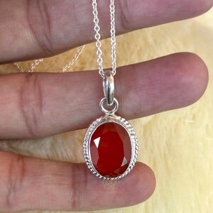 Peut inclure: Un collier en argent avec un pendentif en forme de pierre pr&eacute;cieuse rouge ovale et facett&eacute;e. Le pendentif est encadr&eacute; d'un motif de corde torsad&eacute;e et est suspendu &agrave; une cha&icirc;ne d&eacute;licate.