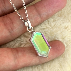 May include: A silver necklace featuring a rectangular, iridescent pendant with a faceted surface. The pendant displays shades of green, yellow, and purple. The chain is a delicate silver link design, and the pendant is held by a silver bail.