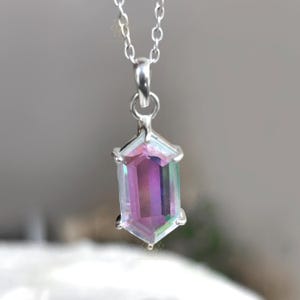 May include: A silver necklace featuring a pendant with a multi-colored, hexagonal gemstone. The gemstone displays hues of purple, pink, and green. The pendant is suspended from a delicate silver chain, creating an elegant and eye-catching piece of jewelry.