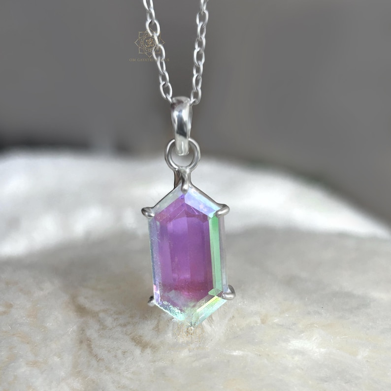 May include: A silver necklace featuring a pendant with a rectangular, iridescent crystal. The crystal displays shades of purple, pink, and green. The pendant is set in a silver frame and hangs from a delicate silver chain. The jewelry is displayed on a soft, white surface.