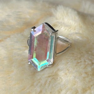 Pu&ograve; includere: Un anello d'argento con una grande gemma rettangolare e iridescente. La gemma mostra uno spettro di colori, tra cui rosa, verde e blu, ed &egrave; incastonata in una semplice fascia d'argento. L'anello &egrave; un gioiello di grande effetto.
