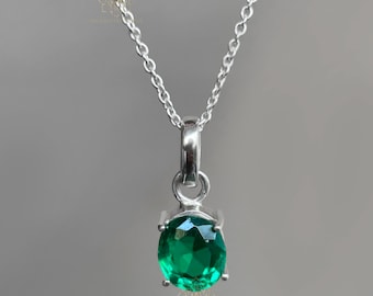 May include: A silver pendant necklace featuring a vibrant, oval-cut emerald green gemstone. The gemstone is held in a four-prong setting and hangs from a delicate silver chain. The necklace is displayed against a neutral background.