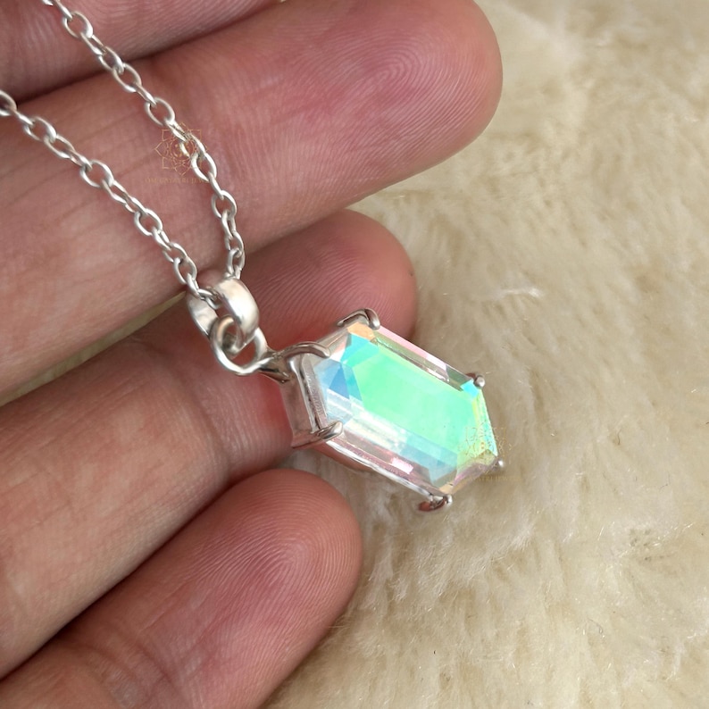 May include: A silver necklace featuring a rectangular iridescent pendant. The pendant has a clear, multi-colored surface that reflects light. The chain is made of small, linked silver pieces.