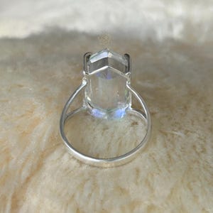 Pu&ograve; includere: Un anello d'argento con una grande gemma trasparente e sfaccettata. La gemma ha una forma rettangolare con una parte superiore a punta. La fascia dell'anello &egrave; in argento lucido. La gemma ha una sottile lucentezza iridescente.