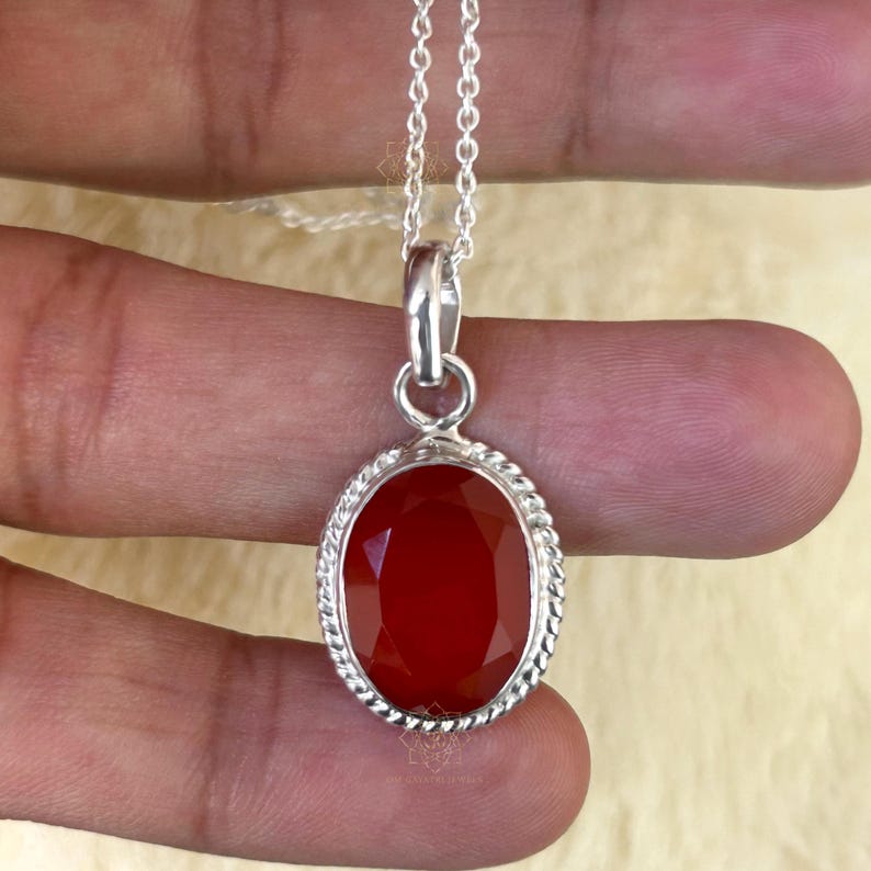Peut inclure: Un collier pendentif en argent avec une pierre pr&eacute;cieuse rouge ovale et facett&eacute;e. La pierre pr&eacute;cieuse est sertie dans un cadre argent&eacute; avec un motif de corde torsad&eacute;e. La cha&icirc;ne du collier est une fine cha&icirc;ne en argent.