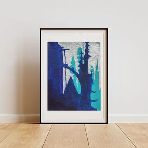 May include: Abstract art print in a black frame. The artwork features a textured silver background with overlapping shapes in shades of blue and teal. The artwork is displayed on a wooden floor against a white wall.