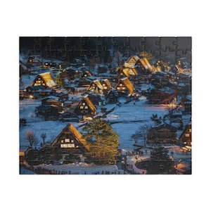 以下が含まれることがあります： 雪に覆われた夜の村のシーンを特徴とする完成したジグソーパズル。パズルは、暗い星空を背景に、照明付きの窓と茅葺き屋根のあるいくつかの家を描いています。パズルは多くの連動するピースでできています。