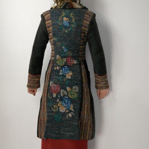 May include: A long, dark gray coat with floral embroidery in red, blue, and green. The coat has long sleeves and a patterned design on the back and sleeves. The bottom half of the person is wearing a long, red skirt.