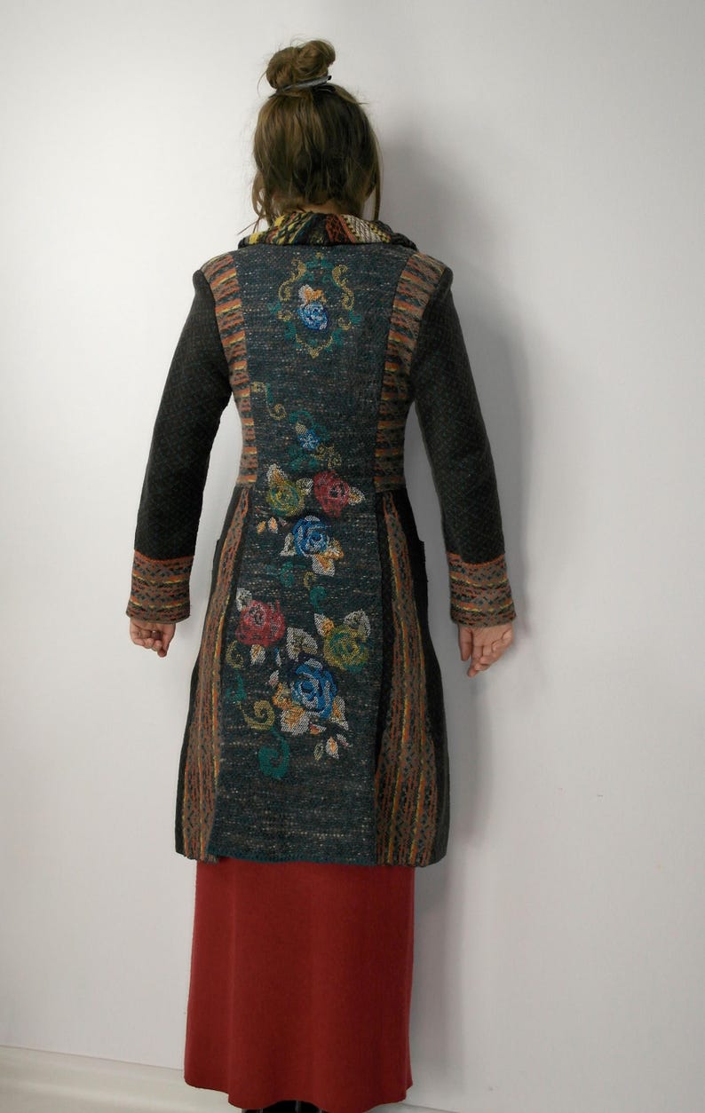 May include: A long, dark gray coat with floral embroidery in red, blue, and green. The coat has long sleeves and a patterned design on the back and sleeves. The bottom half of the person is wearing a long, red skirt.