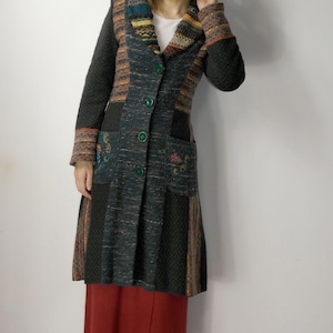 May include: A long, dark green coat with a patchwork design. The coat features a collared neckline, green buttons, and pockets with embroidered floral details. The sleeves and collar have colorful striped patterns. The coat is worn over a red skirt.