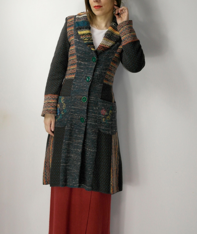 May include: A long, dark green coat with a patchwork design. The coat features a collared neckline, green buttons, and pockets with embroidered floral details. The sleeves and collar have colorful striped patterns. The coat is worn over a red skirt.