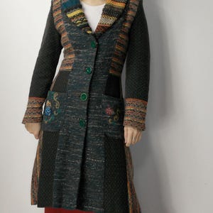 May include: A long, multi-colored coat with a textured design. The coat features a mix of dark green, brown, and orange panels, with embroidered floral details on the pockets. It has a shawl collar and green buttons.