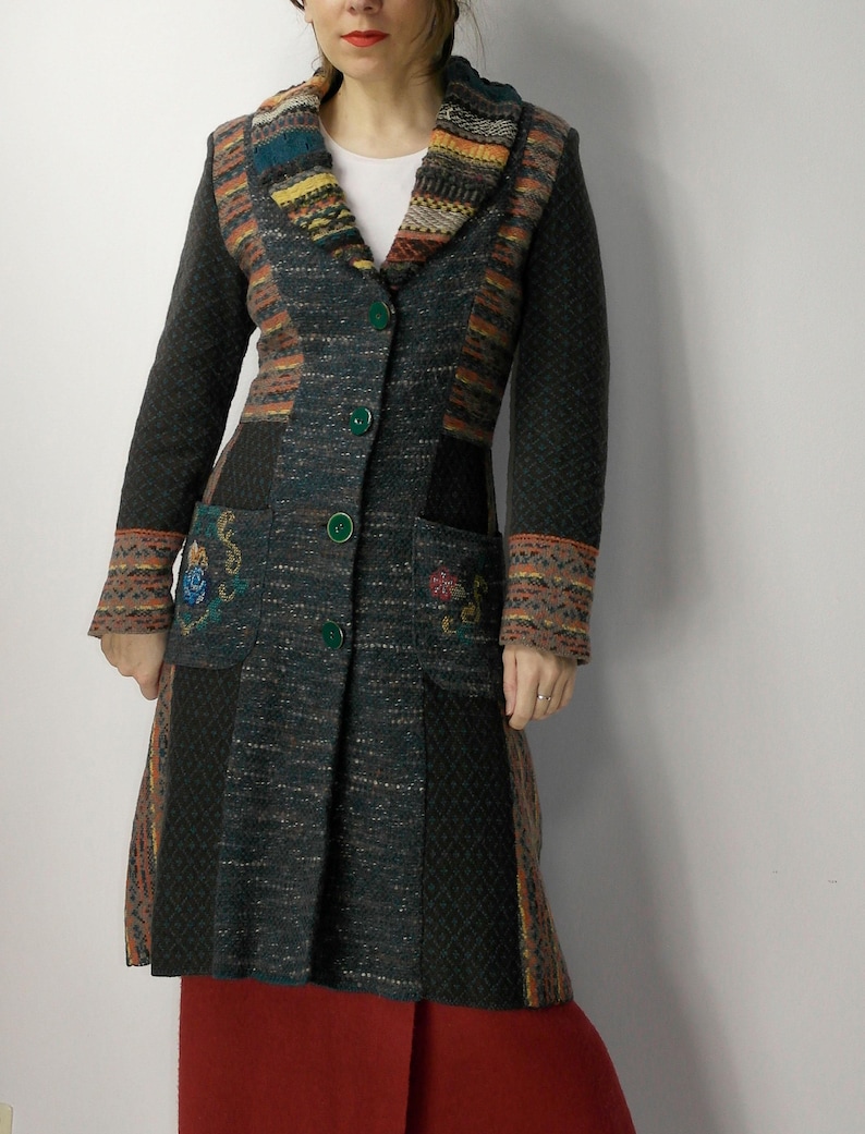 May include: A long, multi-colored coat with a textured design. The coat features a mix of dark green, brown, and orange panels, with embroidered floral details on the pockets. It has a shawl collar and green buttons.