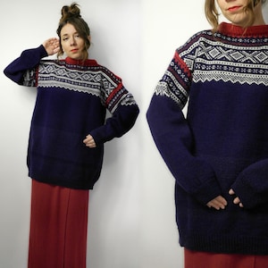 Puede incluir: Un suéter azul marino con cuello rojo y canesú estampado. El canesú presenta diseños geométricos blancos y rojos. El suéter tiene mangas largas y un corte holgado. La modelo lleva una falda roja.