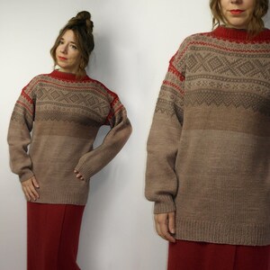May include: A brown sweater with a red collar and shoulder accents. The sweater features a geometric pattern across the chest and upper sleeves. The sleeves are long and the sweater is a loose fit.