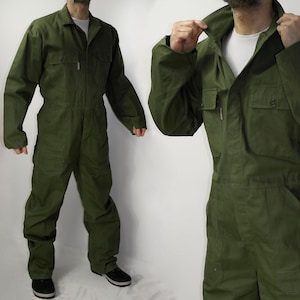 Pode incluir: Um macacão de trabalho verde com gola, mangas compridas e vários bolsos. A peça única tem fecho frontal com zíper e é feita de tecido durável. O modelo está usando sapatos pretos.