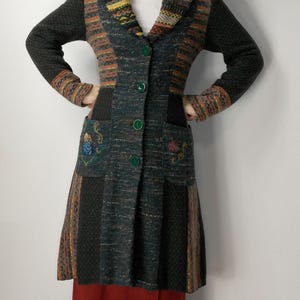 May include: A long, multi-colored knit coat with a unique patchwork design. The coat features a mix of dark green, orange, and brown hues, with embroidered floral details on the pockets. It has a collared neckline and green button closures.
