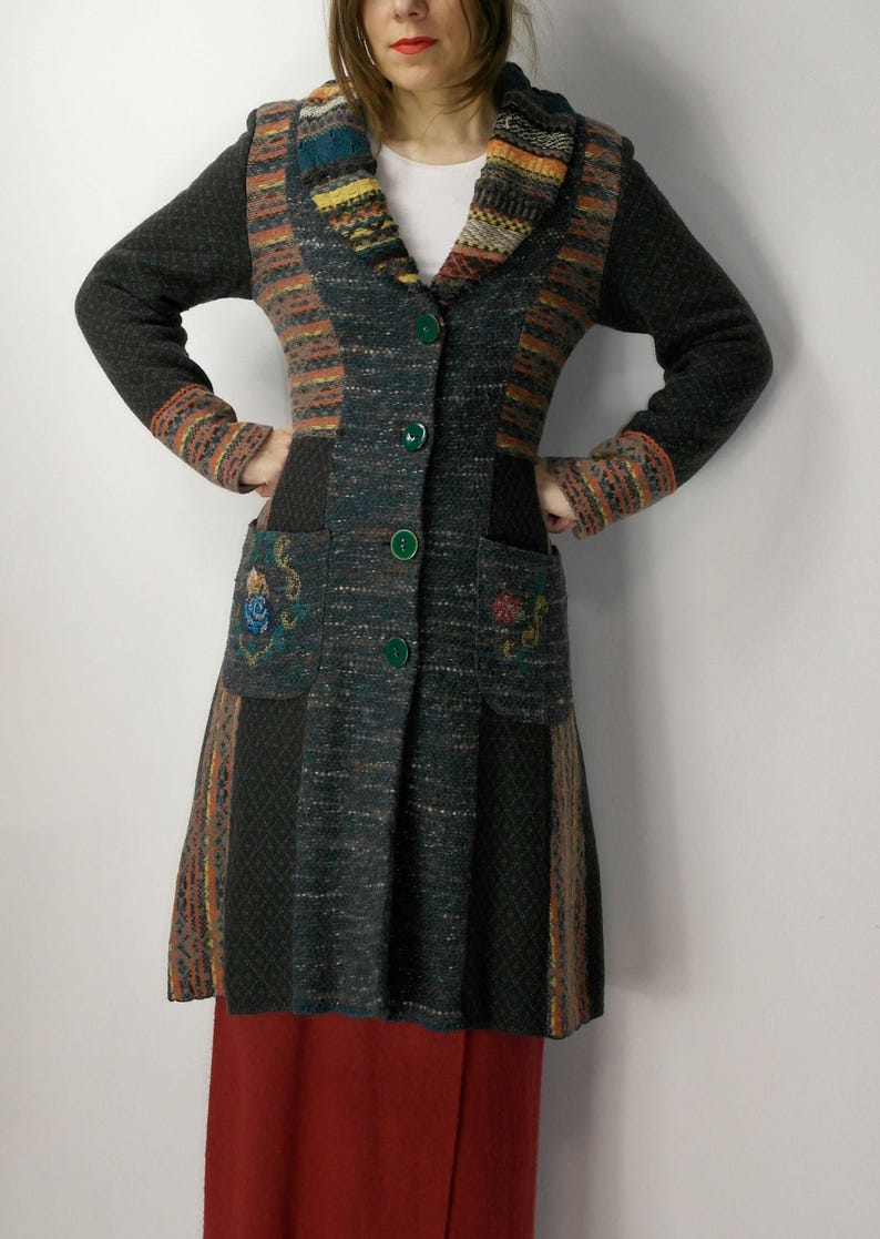 May include: A long, multi-colored knit coat with a unique patchwork design. The coat features a mix of dark green, orange, and brown hues, with embroidered floral details on the pockets. It has a collared neckline and green button closures.