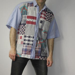 May include: A short-sleeved shirt with a patchwork design on the front and light blue sleeves. The patchwork includes various patterns in red, white, blue, and other colours. The shirt has a classic collar.