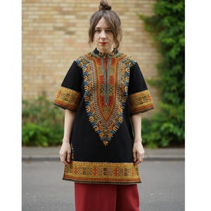 Peut inclure: Tunique noire avec des détails brodés colorés. La tunique présente un col mandarin et des manches courtes. La broderie comprend des nuances de rouge, d'orange, de jaune, de bleu et de vert. La tunique est portée avec un pantalon rouge.