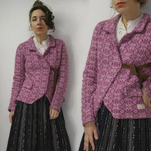 May include: A magenta blazer with a geometric pattern and a brown belt. The blazer has a notched collar and two front pockets. The outfit includes a white blouse and a long black skirt with a striped pattern.