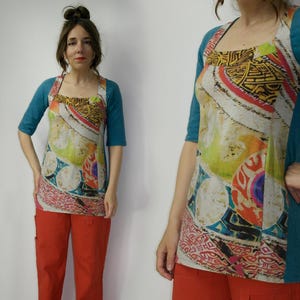 Peut inclure: Un haut tunique coloré avec un col carré et des manches courtes bleu sarcelle. Le haut présente un imprimé vibrant avec des motifs géométriques et abstraits dans des tons de jaune, rouge et bleu. Porté avec un pantalon orange.
