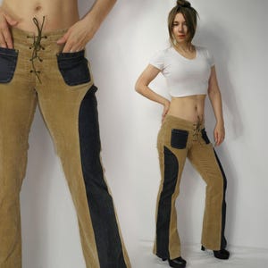 May include: Tan corduroy pants with dark blue denim accents and pockets. The pants feature a lace-up front and a flared leg design. The side panels are dark blue denim. A stylish and unique garment.