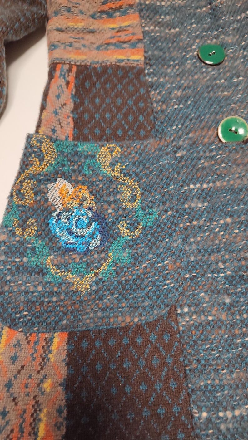 May include: Close-up of a teal and brown patchwork jacket with green buttons. The jacket features a floral embroidery on the pocket and a mix of patterned fabrics. The overall style is bohemian and handcrafted.
