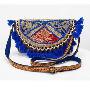 Può includere: Borsa a tracolla ricamata blu e rossa con patta decorativa. La borsa presenta finiture con perline dorate e bianche, nappe blu e una tracolla fantasia. Il design incorpora motivi floreali e geometrici.