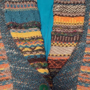May include: A teal and multicolored knit jacket with a large collar. The collar and front panels feature a striped pattern in shades of orange, yellow, brown, and teal. A large green button secures the jacket.