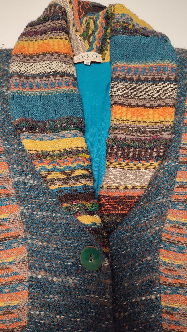 May include: A teal and multicolored knit jacket with a large collar. The collar and front panels feature a striped pattern in shades of orange, yellow, brown, and teal. A large green button secures the jacket.