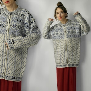 Può includere: Un cardigan color crema con un motivo a fiocchi di neve blu e un'abbottonatura frontale. Il maglione ha maniche lunghe e scollo tondo. Il design include un motivo a rombi nella metà inferiore del maglione.