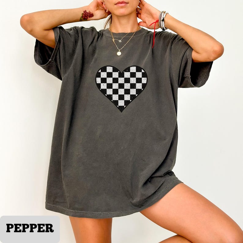 Pu&ograve; includere: T-shirt grigio scuro con un motivo a cuore a scacchi bianchi e neri. La maglietta ha maniche corte e una vestibilit&agrave; ampia. La parola "PEPPER" &egrave; stampata in basso nell'immagine.