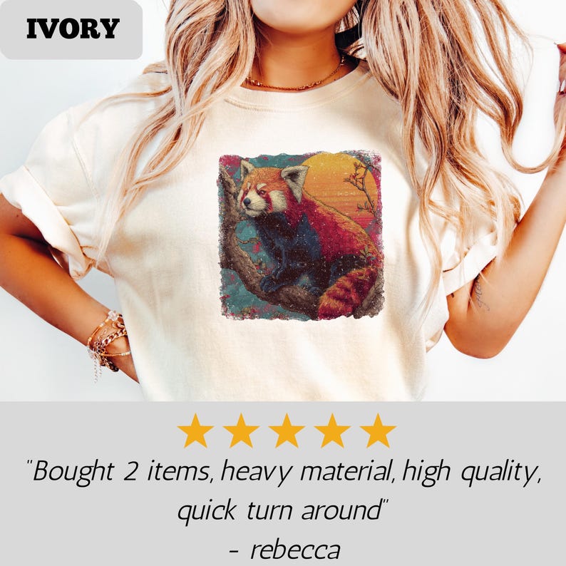 Puede incluir: Camiseta de color marfil con un gr&aacute;fico vibrante de un panda rojo posado en una rama contra un fondo de puesta de sol. La camiseta tiene cuello redondo y mangas cortas. La palabra "IVORY" est&aacute; impresa en la parte superior.
