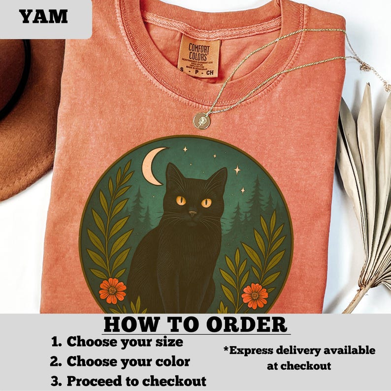 May include: A coral-colored t-shirt featuring a circular graphic of a black cat with yellow eyes, a crescent moon, and a forest scene. The shirt has a Comfort Colors tag and a gold necklace. Text on the shirt reads "HOW TO ORDER".