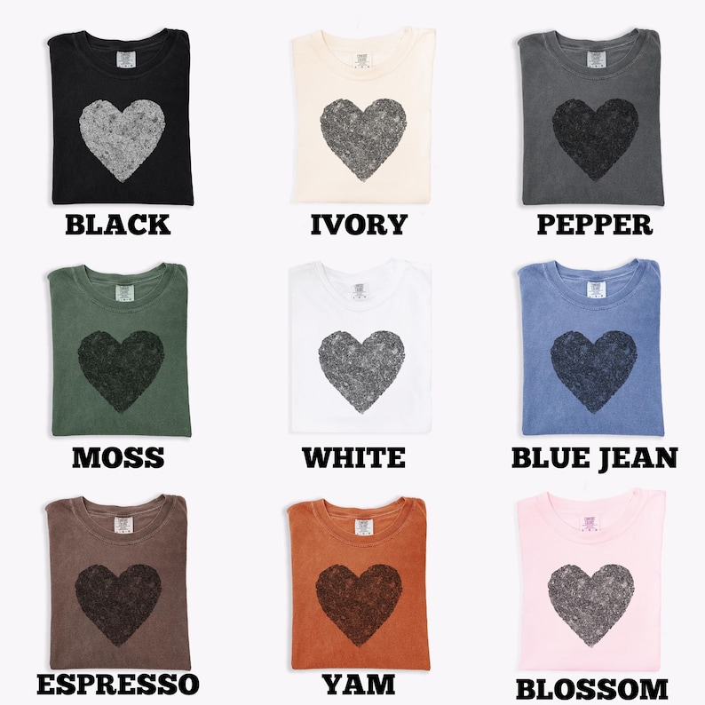 K&ouml;nnte beinhalten: Neun verschiedenfarbige T-Shirts, jedes mit einem gro&szlig;en Herz-Grafik. Farben sind Schwarz, Elfenbein, Pfeffer, Moos, Wei&szlig;, Blue Jean, Espresso, Yam und Blossom. Jedes Shirt hat den Farbnamen darunter gedruckt.