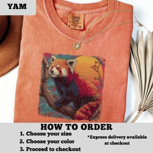 Puede incluir: Una camiseta de color coral con un gr&aacute;fico de un panda rojo en una rama con un fondo de puesta de sol. La camiseta tiene cuello redondo y mangas cortas. Un collar dorado con un colgante est&aacute; sobre la camiseta. El texto "HOW TO ORDER" es visible.
