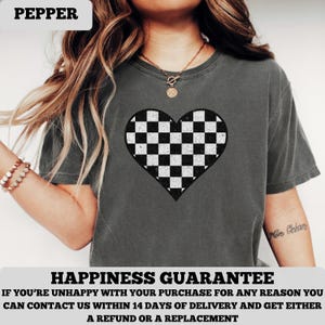 Pu&ograve; includere: T-shirt grigio scuro con un motivo a cuore a scacchi bianchi e neri. La maglietta ha maniche corte e girocollo. La parola "PEPPER" &egrave; nella parte superiore dell'immagine.