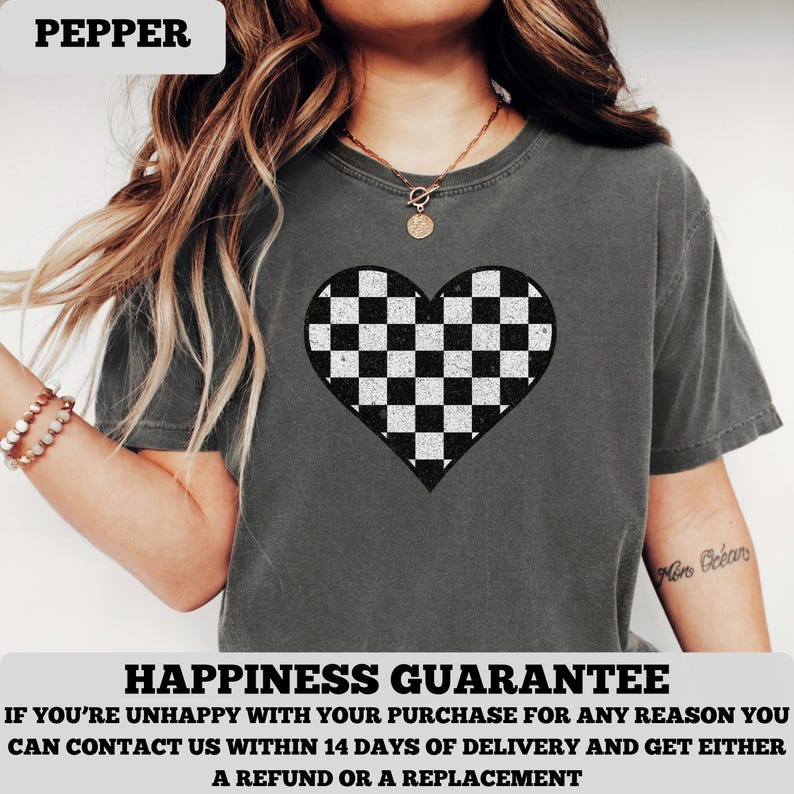Pu&ograve; includere: T-shirt grigio scuro con un motivo a cuore a scacchi bianchi e neri. La maglietta ha maniche corte e girocollo. La parola "PEPPER" &egrave; nella parte superiore dell'immagine.