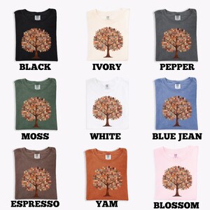 May include: Nine different colored t-shirts, each featuring a tree design with a mosaic-like pattern in the tree's crown. The shirts are in various colors, including black, ivory, pepper, moss, white, blue jean, espresso, yam, and blossom.