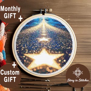 Könnte beinhalten: Ein Kreuzstich-Stickrahmen mit einem großen weißen Stern-Design vor blau-goldenem Hintergrund. Der Text "Monthly GIFT +" und "+ Custom GIFT" sind sichtbar. Der Markenname "Story in Stitches" ist ebenfalls zu sehen.
