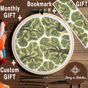 May include: A cross-stitch embroidery kit featuring a green and white tree branch design. The kit includes a round wooden hoop, a matching bookmark, and the text "Monthly Gift" and "Custom Gift". The brand name "Story in Stitches" is also visible.
