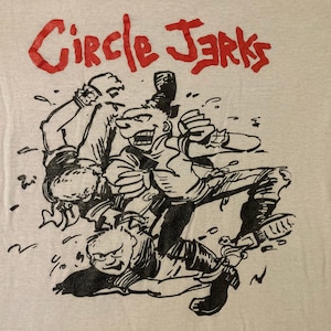 May include: A light gray t-shirt with a black and white cartoon graphic of two figures wrestling. The text "Circle Jerks" is printed in red above the graphic.