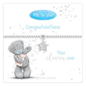 Puede incluir: Una pulsera de cuentas bañada en plata con un dije en forma de estrella con cristales transparentes. La tarjeta muestra un oso de peluche gris, el texto "ME TO YOU", "CONGRATULATIONS" y "You clever ONE", con texto bañado en plata abajo.