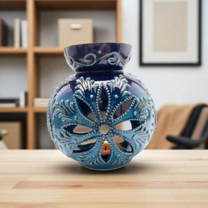 May include: A blue and turquoise ceramic essential oil diffuser with a floral design. The spherical diffuser has cut-out patterns and a candle inside, creating a warm glow. The top is a darker blue with decorative swirls.