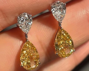 May include: A pair of elegant drop earrings featuring pear-shaped yellow and white diamonds. The earrings have a silver-colored metal setting, with a white diamond at the top and a yellow diamond below.